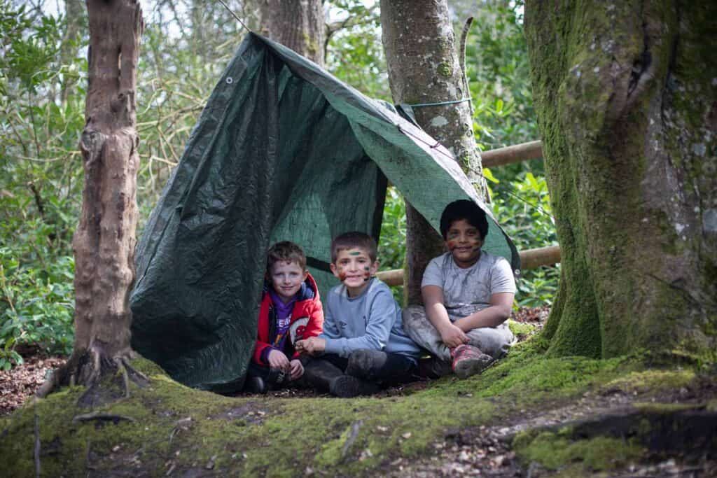 Children building a den together in the forest, enjoying outdoor activities at our holiday club