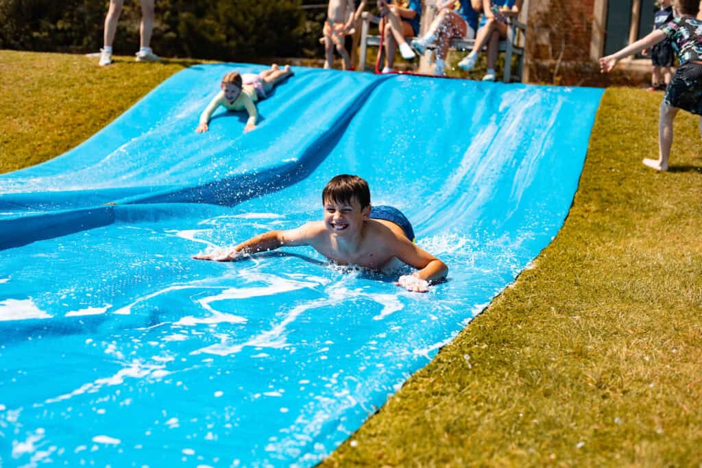 A boy aged 7-10 sliding down our DIY water slide at Forres Sandle Manor, splashing around in this fun activity.