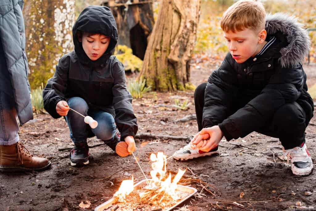 Two boys aged 6-9 holding toasty marshmallows over an open fire