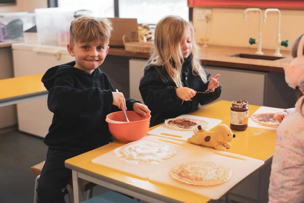 a boy aged 5-8 mixing his pancake mixture with a happy grin. 