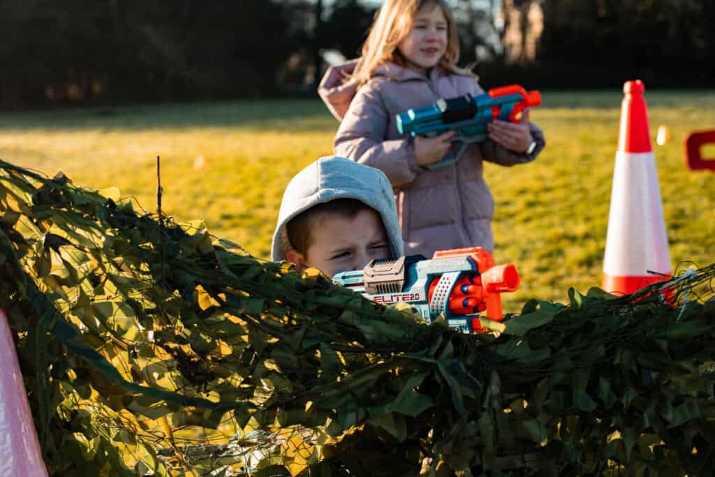 A child aged 8 participating in nerf wars activities, hiding behind a camouflage. 