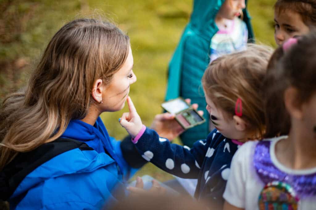 A girl finger painting some face paint on one of our friendly team leaders. our leaders love making these activities feel special.