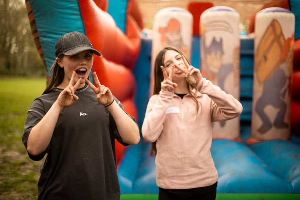 two girls aged 12-15 holding their hands up in piece signs after completing our obstacle course activity.